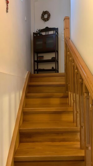 A wooden staircase with a wooden handrail, leading to a room with a dark wooden cabinet and a wreath on the wall.
