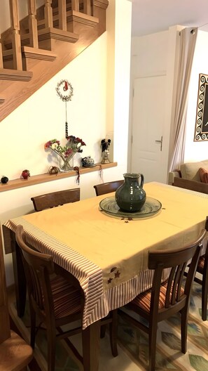 Un comedor con una mesa de madera, sillas, un florero con flores, un adorno en la pared y una escalera.