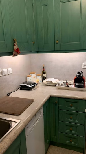A kitchen with green cabinets, a coffee maker, a bottle of wine, and a toaster.