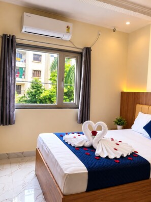 Habitación de hotel con cama, ventana con cortinas, aire acondicionado, planta en maceta y lámpara fijada a la pared.