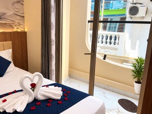 Una habitación de hotel con cama, un balcón con planta en maceta y vistas al exterior.
