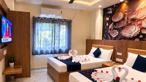 Habitación de hotel con dos camas, televisión, ventana con cortinas y un mural floral en la pared.
