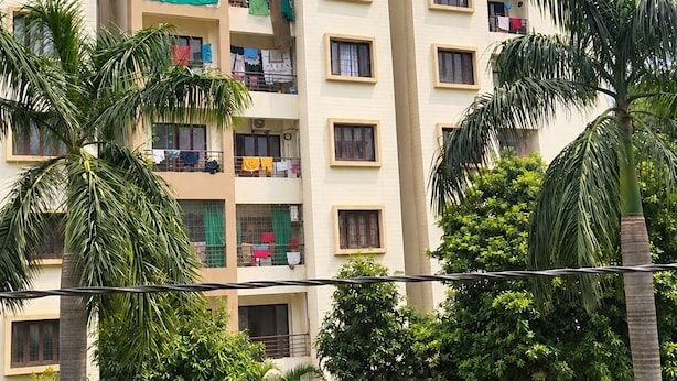 Un edificio residencial de varios pisos con balcones, rodeado de abundante vegetación y palmeras.