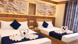 Habitación de hotel con dos camas, cada una decorada con toallas dispuestas en forma de corazón y pétalos de rosa.