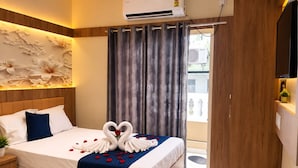 Habitación de hotel con cama, mesita de noche, aire acondicionado instalado en la pared, ventana con cortinas y puerta.