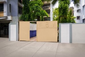 A gated entrance with a beige gate and a blue curtain, leading to a building with multiple balconies and greenery. - Luxury Mkni House (Mumbai)