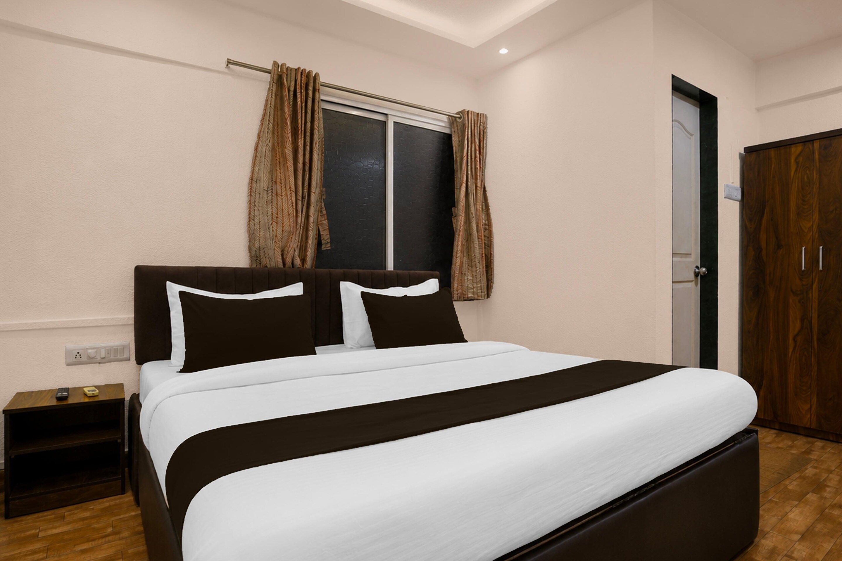 A bedroom with a bed, a nightstand, a wardrobe, and a window with curtains.