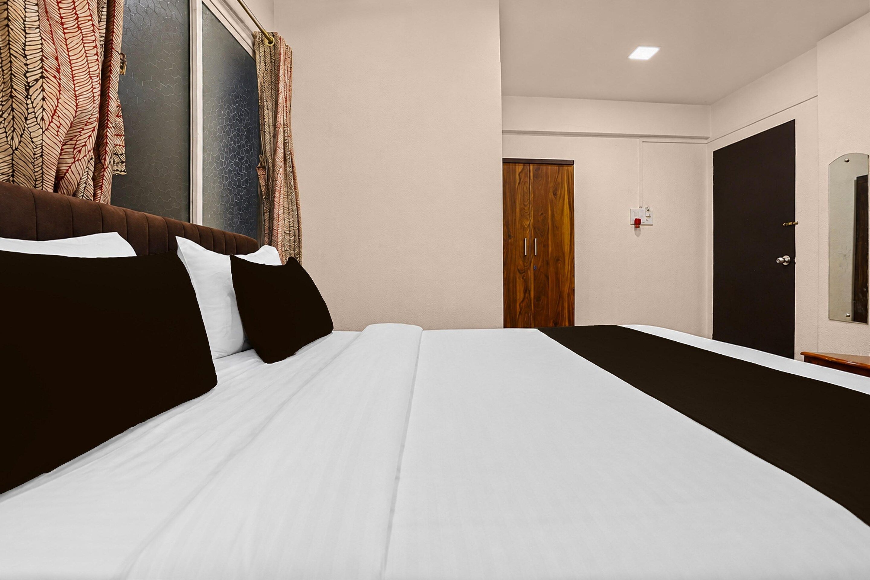 Habitación de hotel con cama, armario de madera, puerta y ventana con cortinas.