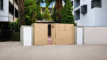 Una entrada cerrada con un portón metálico y una puerta, rodeada de árboles y edificios.