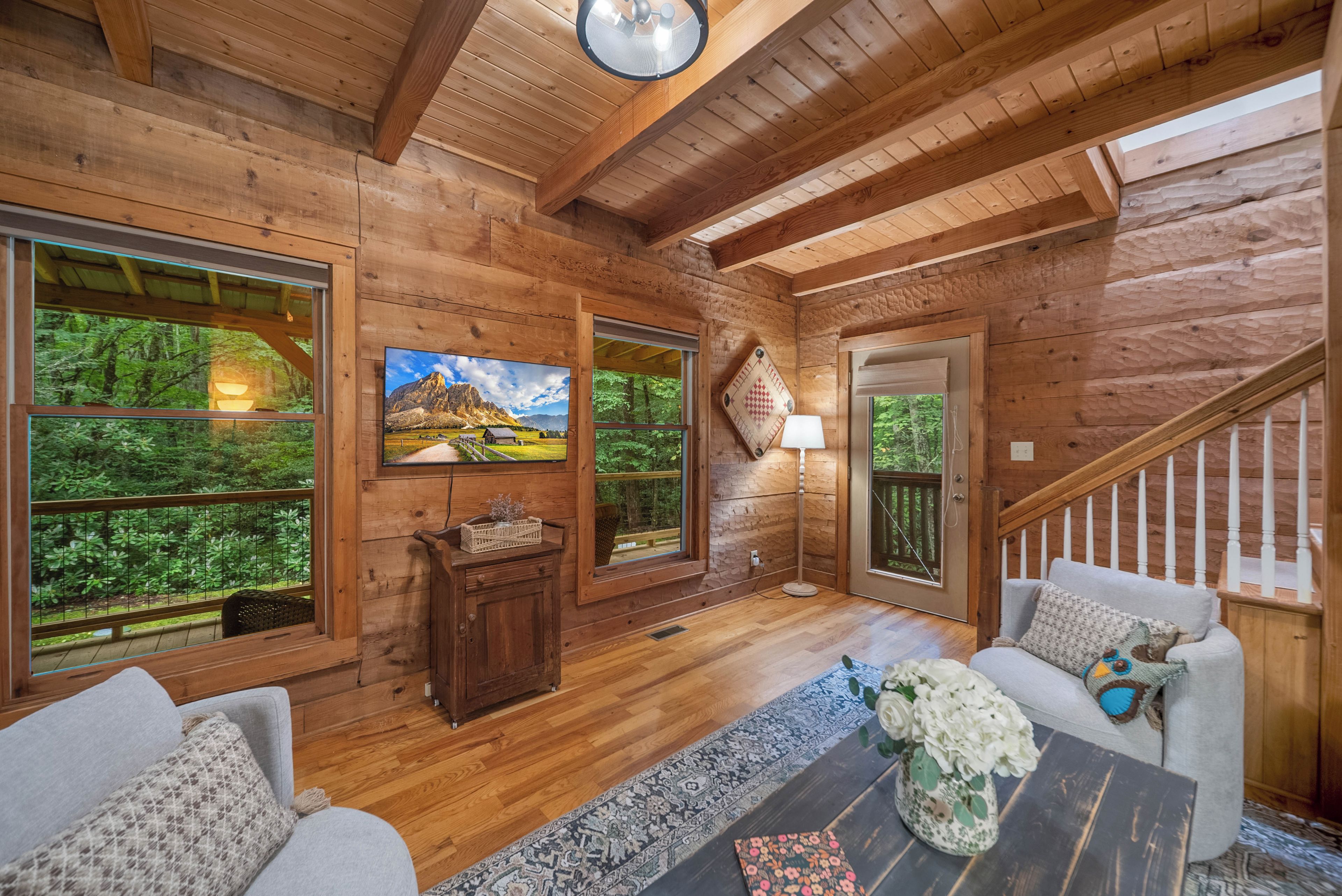 A wooden cabin interior with a sofa, a coffee table, a TV, and a staircase.