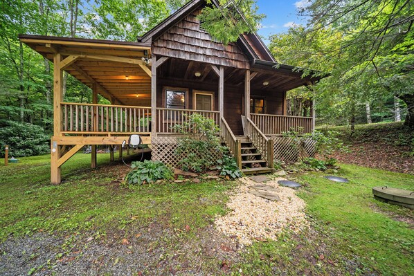 Une cabane en bois dotée d’une véranda, d’une terrasse couverte et d’un chemin de gravier menant à l’entrée.