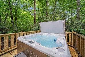 Un bain à remous situé dans un espace boisé, avec une terrasse en bois et une rambarde en bois.