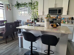 A modern kitchen with a central island, bar stools, a microwave, and various kitchen appliances. - Charming and Cozy Home (Edmonton)