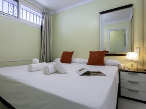 Ein Hotelzimmer mit Bett, Kissen, einem Nachttisch mit Lampe, einem Spiegel und einem Fenster mit Vorhängen.