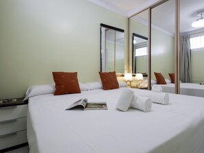 A hotel room with a bed, pillows, a mirror, a bedside table, and a window. - Sunstay Flat Cortijera Mijas (Mijas)
