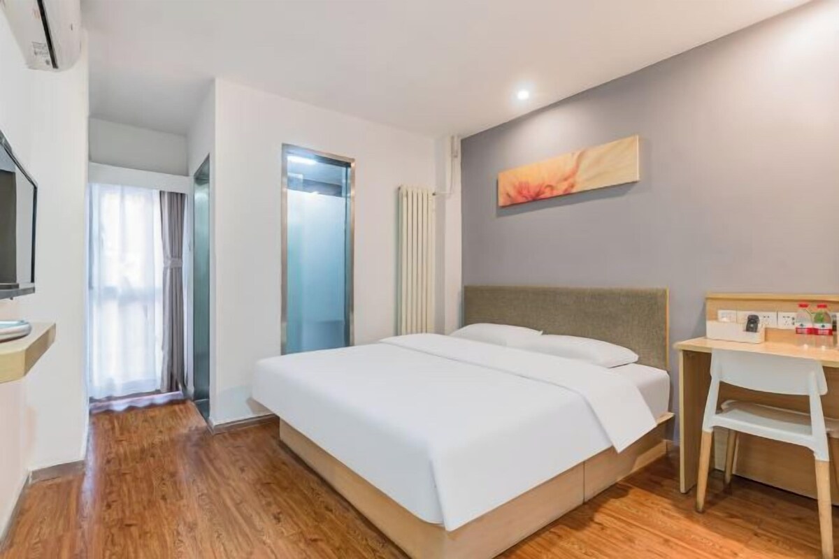 A hotel room with a bed, a desk, a chair, a television, and a bathroom door.