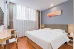 Et hotelværelse med seng, skrivebord, stol, natbord og et maleri på væggen.