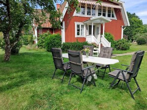 Ein rotes Haus mit weißem Veranda und einem Esstisch mit Stühlen im Hof.