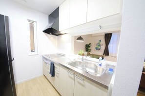 A modern kitchen with a dishwasher, sink, and a black range hood. - Homeward Shinkawa D (Sapporo)
