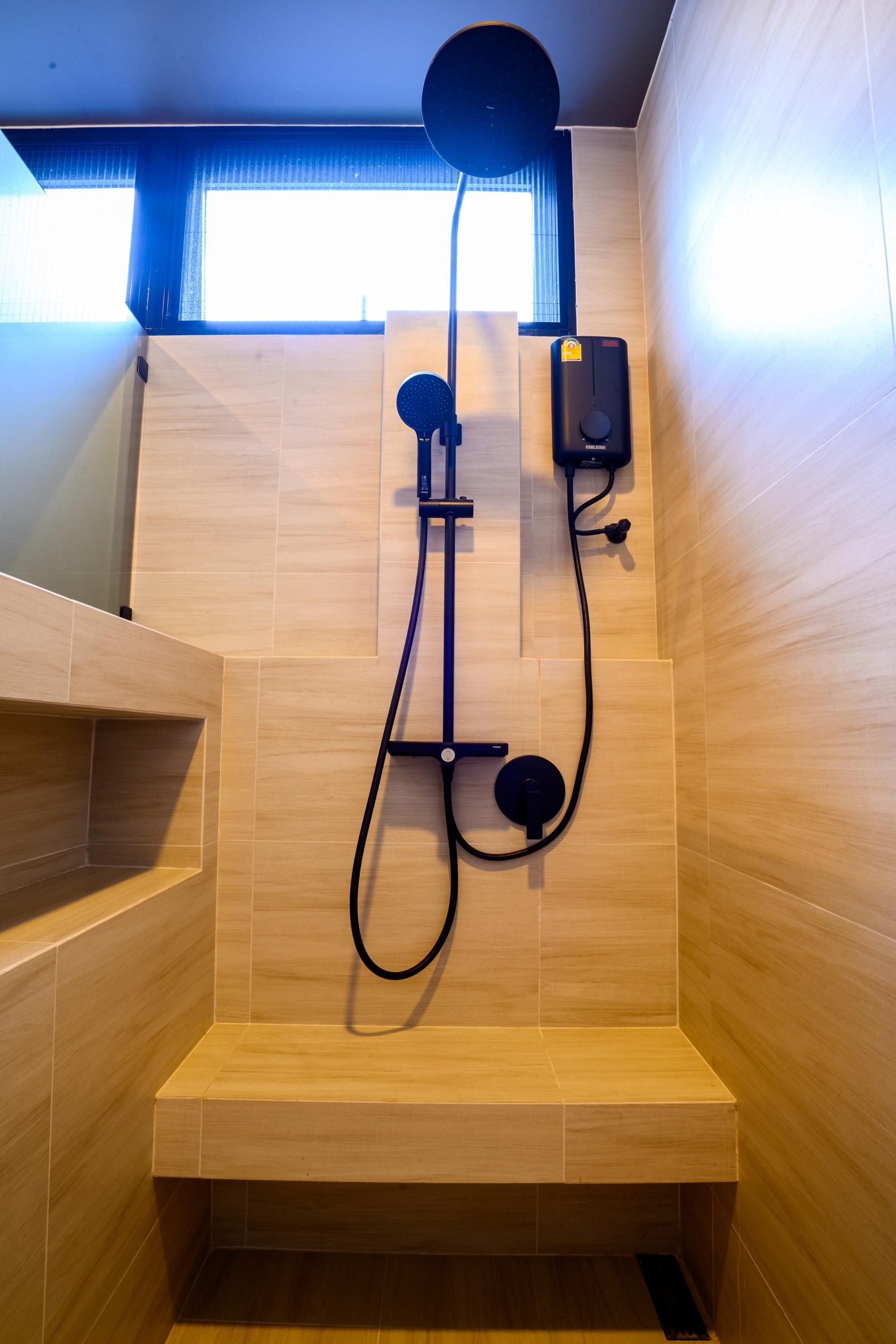 A shower area with a handheld showerhead, a wall-mounted control panel, and a bench.