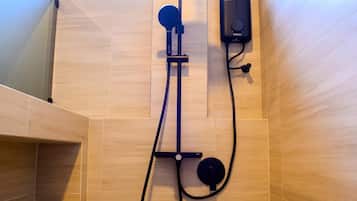 A shower area with a handheld showerhead, a wall-mounted control panel, and a bench.