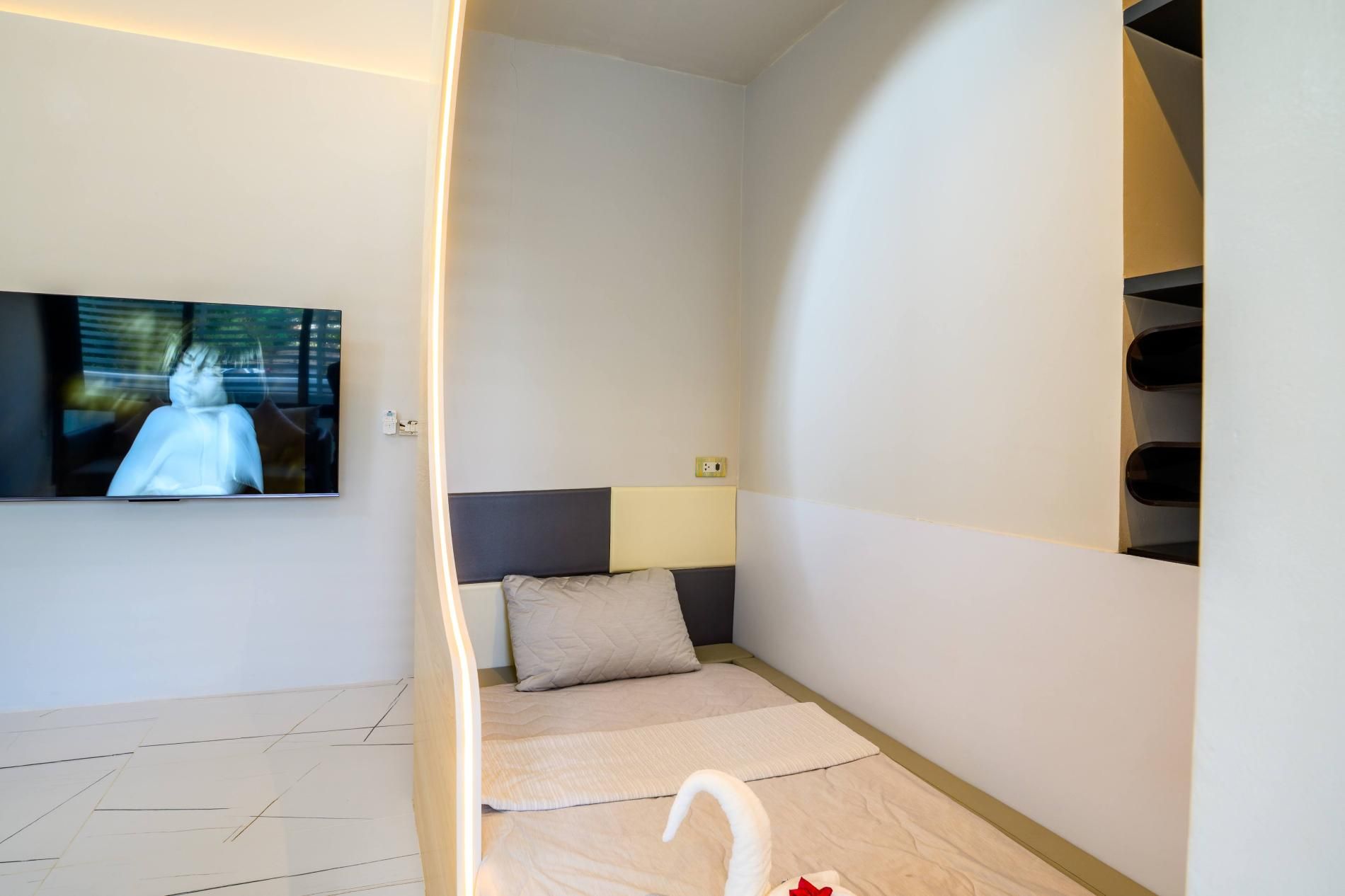 Un dormitorio moderno con una cama, un televisor montado en la pared y una estantería empotrada.