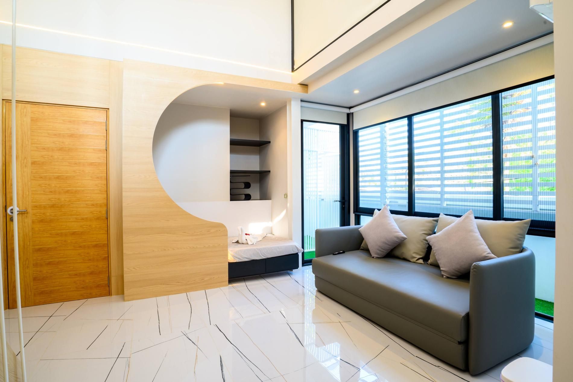 Una sala moderna con un sofá, una puerta de madera y un ventanal con persianas.