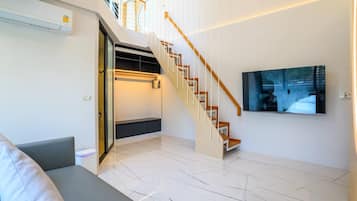 A modern living room with a staircase, a flat-screen TV, and a built-in bench.