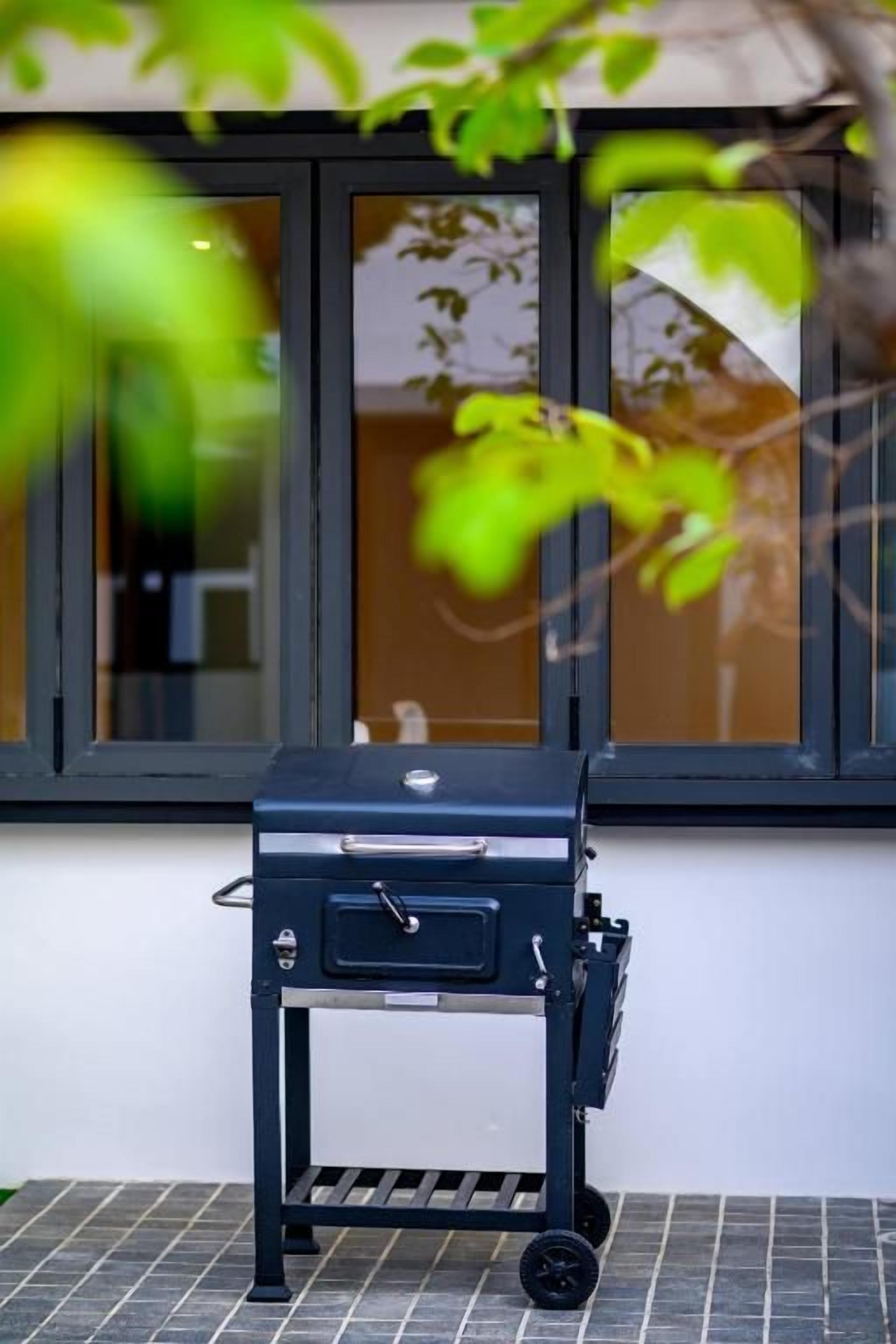 Un barbecue portatif sur roulettes, placé devant une fenêtre donnant sur un immeuble.