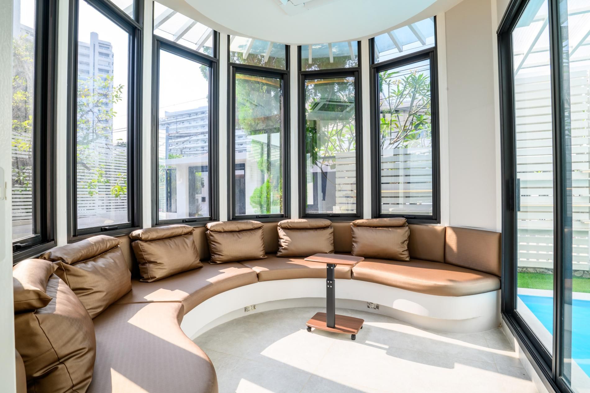 Un intérieur moderne avec un canapé d’angle aux lignes courbes, une petite table et de grandes fenêtres donnant sur l’extérieur.