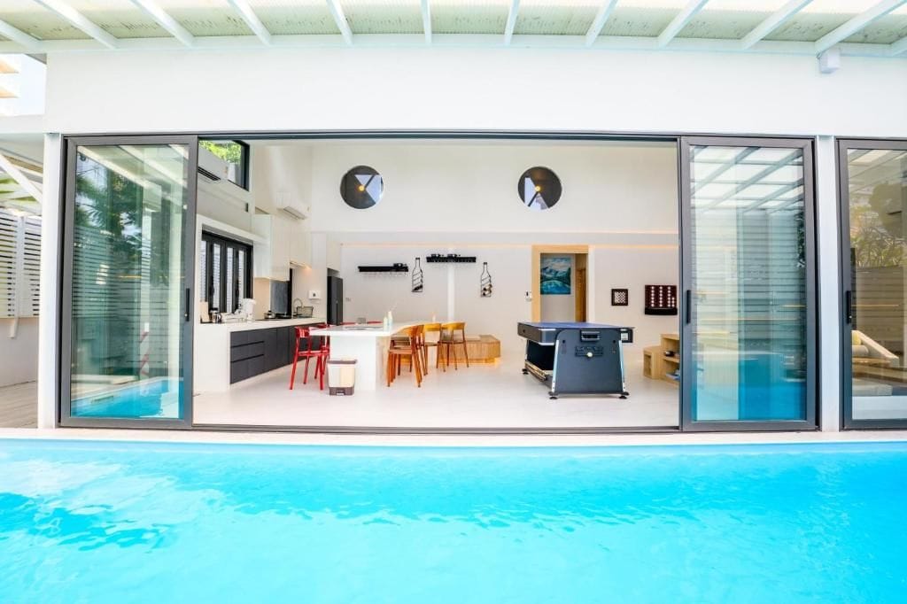 A modern kitchen with a dining area, a pool, and a sliding glass door leading to a living space.