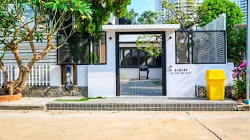 A modern building entrance with a black door, a small outdoor seating area, and a yellow trash bin.