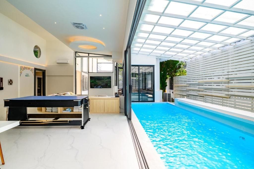 Una piscina interior moderna con techo iluminado por el sol y una mesa.