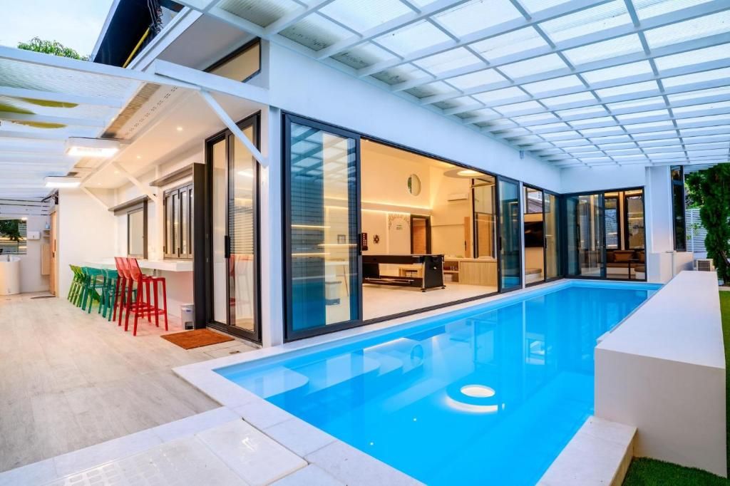 Une maison moderne dotée d’une piscine, de portes vitrées et d’une terrasse avec des chaises.
