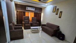 A modern living room with a sofa, chairs, a coffee table, and a ceiling fan. - Hotel Guru Inn (Nanded)