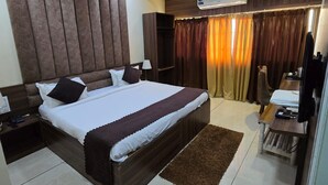 A hotel room with a large bed, a ceiling fan, an air conditioning unit, a vanity with a mirror, and a small table with a lamp. - Hotel Guru Inn (Nanded)