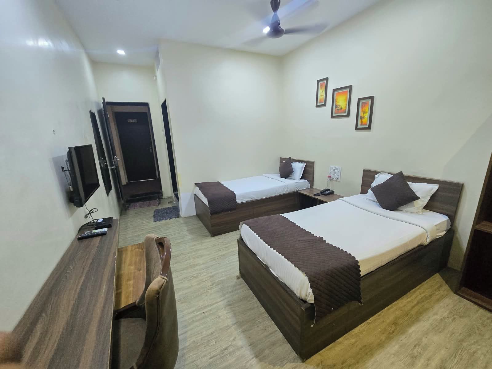 Habitación de hotel con dos camas, un escritorio, una silla, un televisor y una puerta.