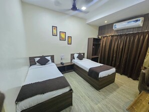 A hotel room with two single beds, a wardrobe, an air conditioning unit, and a curtain.