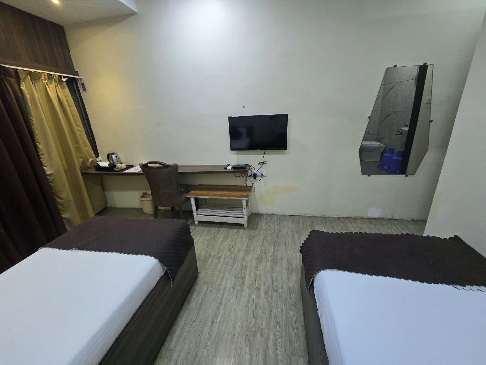 A hotel room with two beds, a desk with a chair, a television, and a bathroom with a mirror.
