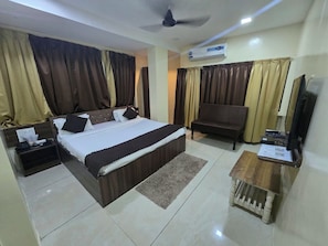 A bedroom with a bed, a chair, a desk, a television, and an air conditioning unit.