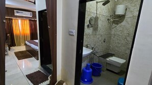 A bathroom with a shower, sink, and toilet. There are two blue buckets and a white trash bin. - Hotel Guru Inn (Nanded)