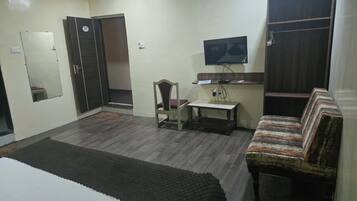 Un dormitorio con cama, una silla, una mesita, un televisor y un armario.