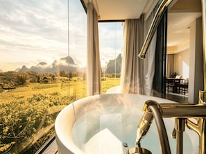 Un baño moderno con una bañera grande, vistas a un paisaje montañoso y un comedor visible a través de la ventana.