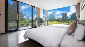A hotel room with a large bed, a chair, and a view of a mountainous landscape through floor-to-ceiling windows. - Yangshou Mountain Vista Courtyard (Guilin)