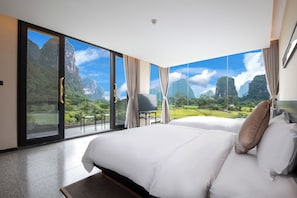 Ein Hotelzimmer mit einem großen Bett, einem Sessel und Blick auf eine gebirgige Landschaft durch raumhohe Fenster.