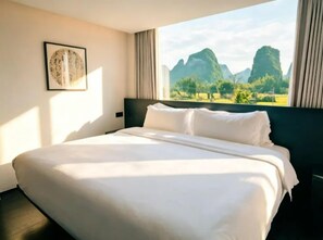 A hotel room with a large bed, a view of mountains, and a framed picture on the wall.