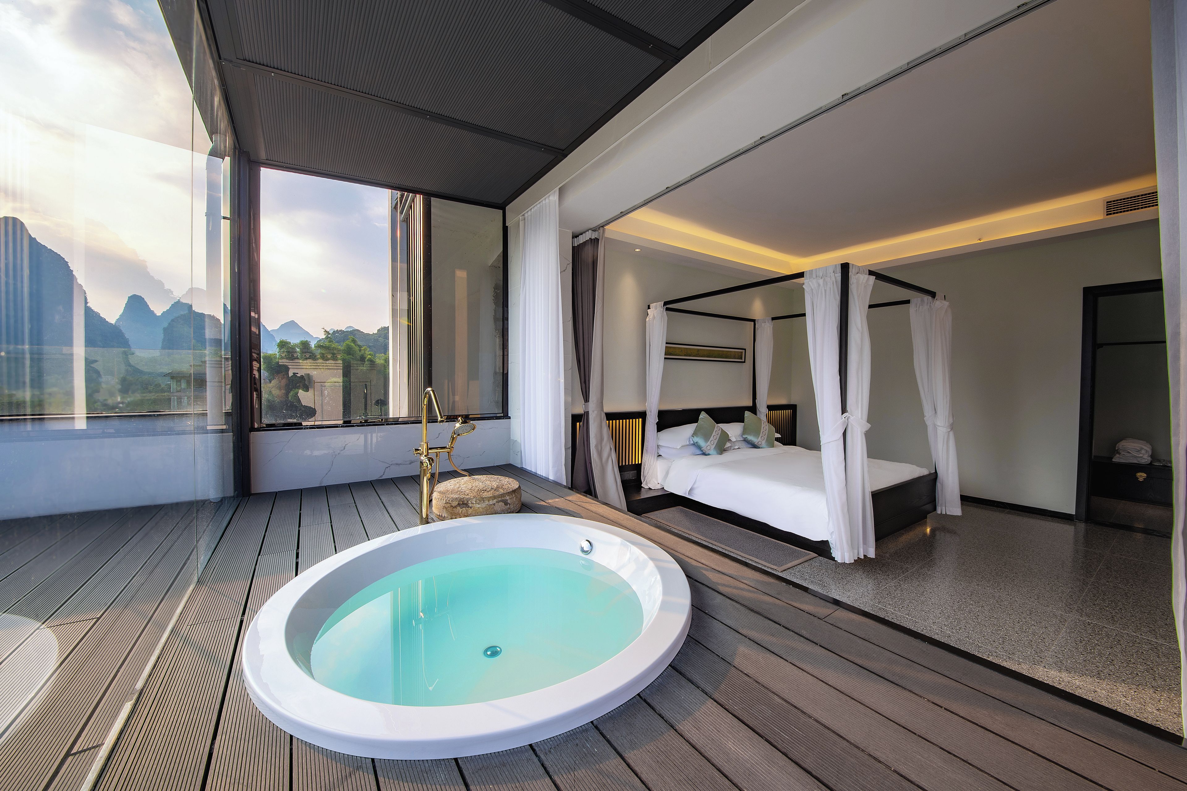 Un dormitorio moderno con cama con dosel, un baño separado con bañera de hidromasaje y vistas a las montañas a través de amplias ventanas.