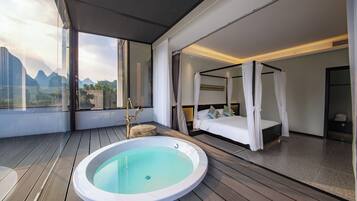 Un dormitorio moderno con cama con dosel, un baño separado con bañera de hidromasaje y vistas a las montañas a través de amplias ventanas.