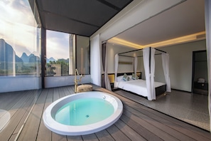 Ein modernes Schlafzimmer mit einem Himmelbett, einem separaten Badezimmer mit Whirlpool und Blick auf Berge durch große Fenster.