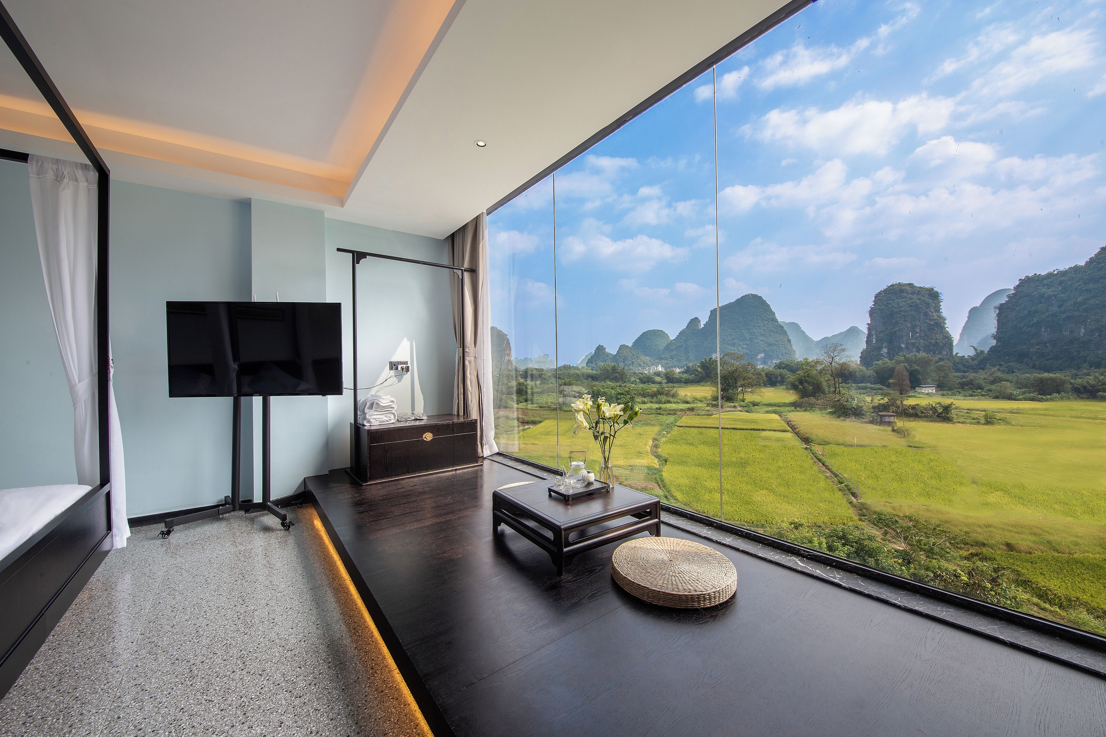 A modern room with a large window, a flat-screen TV, a dark wooden floor, and a small table with a vase.